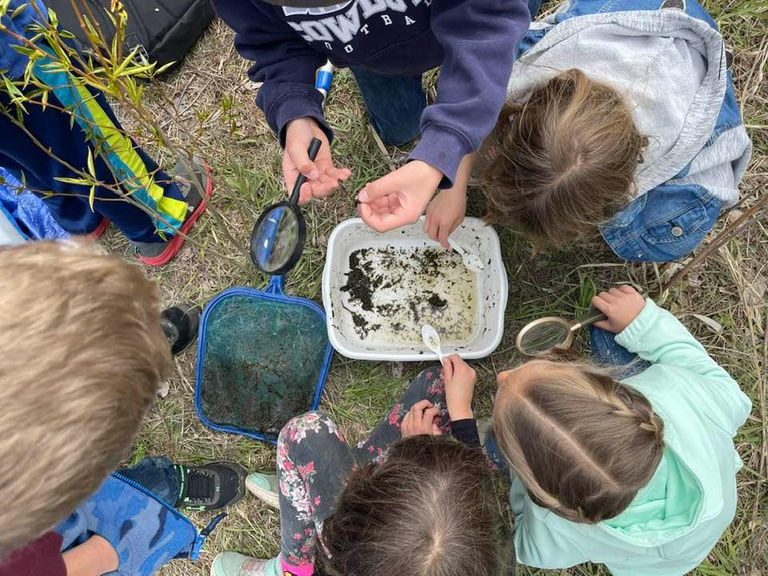 Photo of group of Damman students gathered around with magnifying glasses while on field trip.  